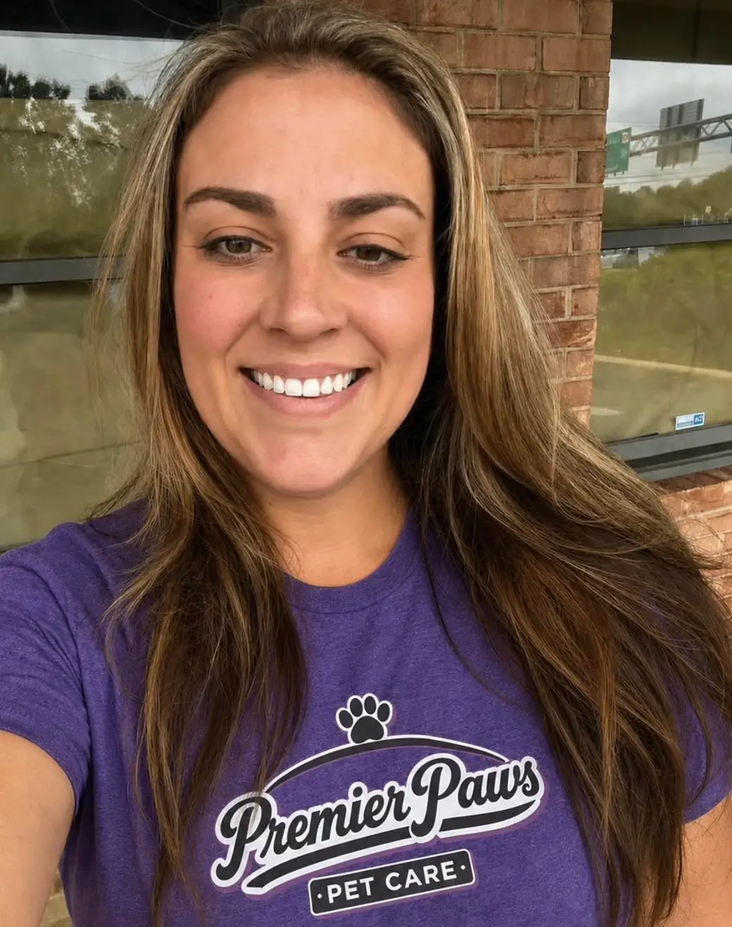 Jessie smiling in a purple Premier Paws t-shirt in front of a brick wall