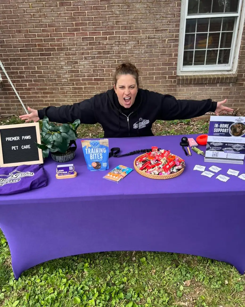 Team member striking a playful arms-wide pose behind the purple Premier Paws event table