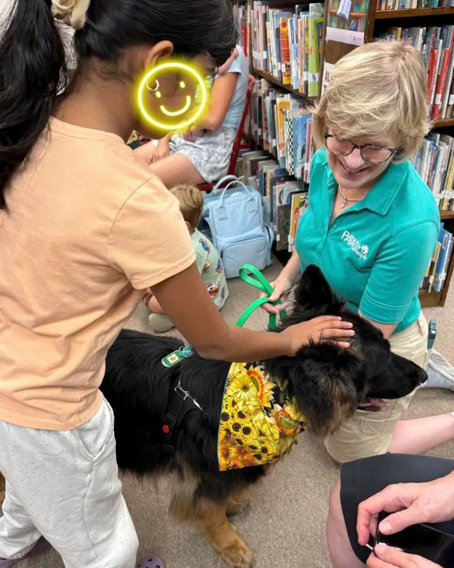 Children practicing gentle petting on a black shepherd mix in a sunflower bandana at a library class